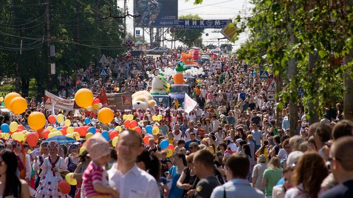 Große Menschenmenge bei einem Umzug mit bunten Ballons und Festwagen.