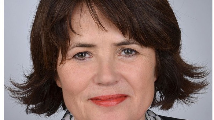 Eine Frau mit kurzem braunen Haar und rotem Lippenstift lächelt in die Kamera.