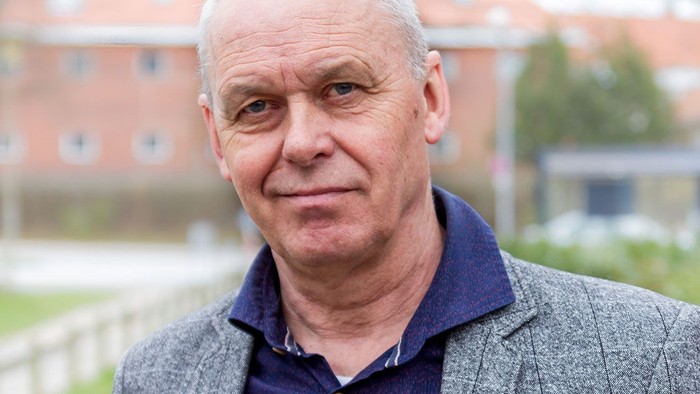 En middelalderlig bygning med røde tag og en mand i en grå jakke og blå skjorte.