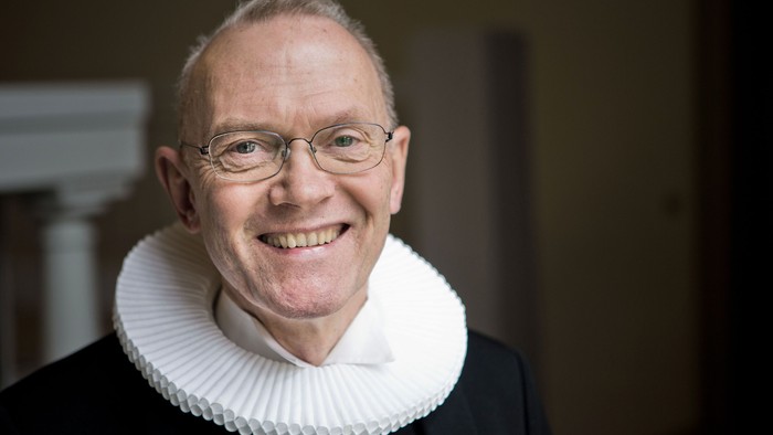 En glad mand med hvid krage og briller.