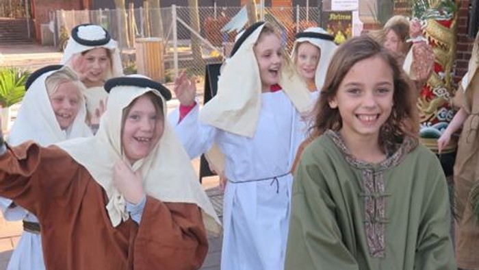 En gruppe børn i historiske kostumer danser og leker på en gade.