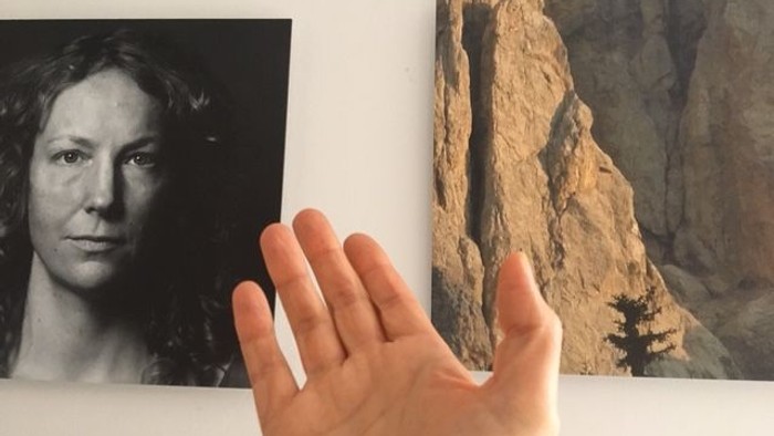 Eine Hand zeigt auf zwei Fotos, eines mit einer Frau und eines mit einer Felswand