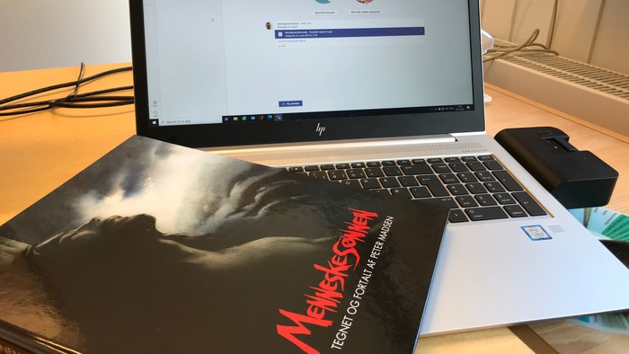 En HP laptop på skrivebord med en bog og en papirnotat.