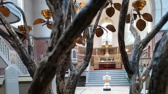 En kirkeinterior med alter og bænke, set fra gennem grene.
