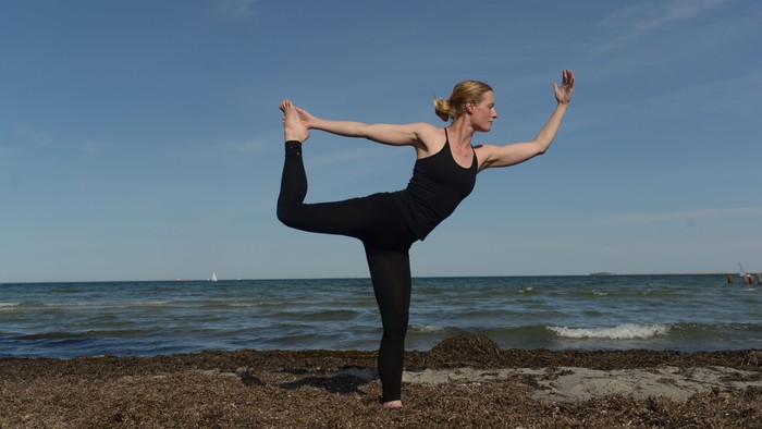 En kvinde udfører yoga på en klippe ved stranden.