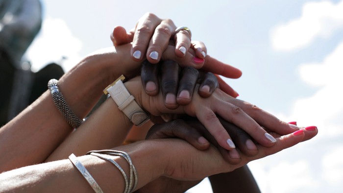 Mehrere Hände bilden einen Stapel, Schmuck ist zu sehen, Himmel im Hintergrund