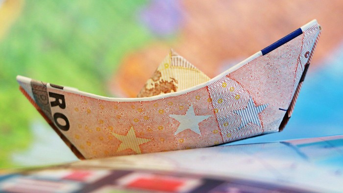 Ein Origami-Boot aus einem Euro-Schein mit Spielzeugfiguren darin.