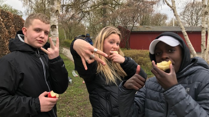 Tre unge mennesker spiser æbler i en park.