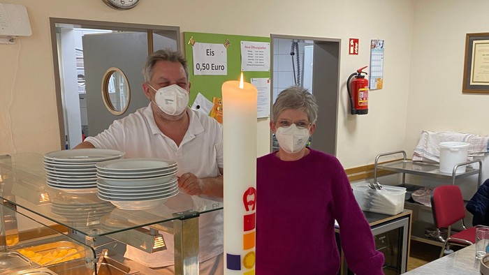 Zwei Personen hinter Theke in Kantine, eine mit Mundschutz