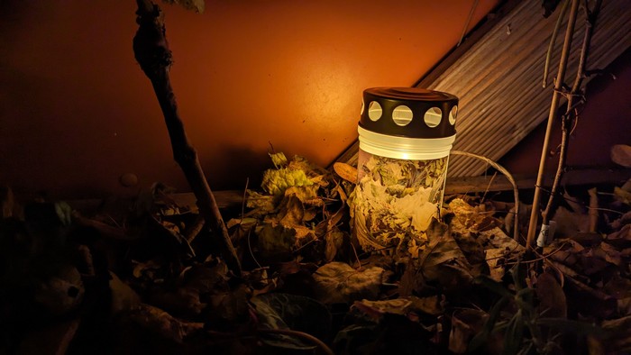 Eine Laterne steht auf einem Haufen aus Blättern und Ästen in einem dunklen Bereich.