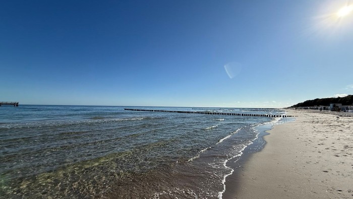 Ein ruhiger Strand mit klarem Wasser und einem Pier in der Ferne unter einem klaren blauen Himmel