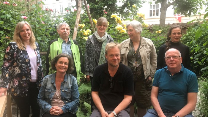 En gruppe af ni personer sidder og står i en trækirkegård, alle smiler til kameraet