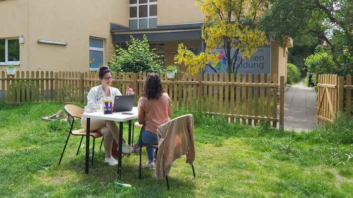 Zwei Personen sitzen im Garten vor einem Haus und arbeiten an einem Laptop.