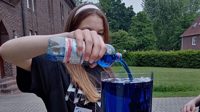 Mädchen gießt blaue Flüssigkeit in Zylinder