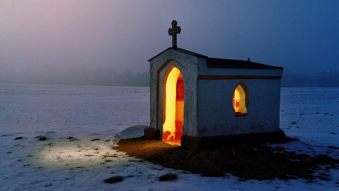 Kleine, beleuchtete Kapelle im Schnee bei Dämmerung