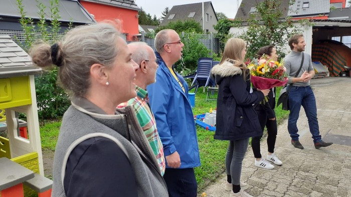 Eine Gruppe von Menschen steht in einem Garten, eine Frau hält Blumen.