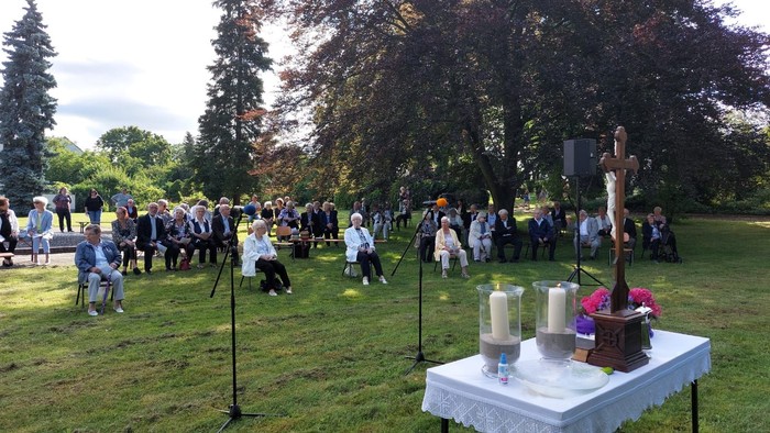 Eine Gruppe von Menschen nimmt an einer Freiluftmesse teil, bei der ein Tisch mit Kerzen und einem Kruzifix geschmückt ist.