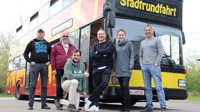 Eine Gruppe von Menschen steht vor einem gelben Doppeldeckerbus mit der Aufschrift 