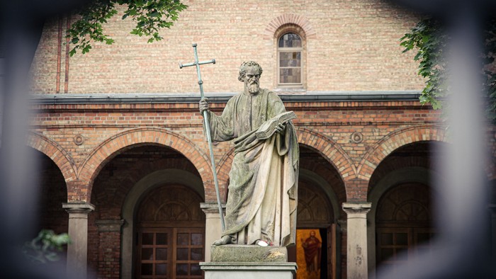 Statue eines Mannes mit Kreuz vor Backsteingebäude
