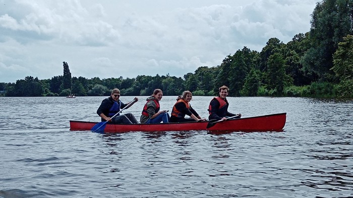 Vier Personen paddeln in einem roten Kanu auf einem See.