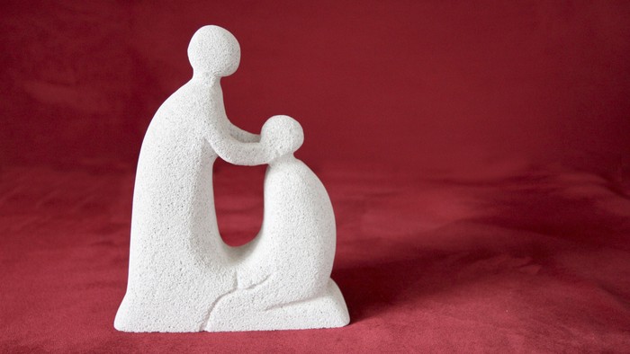 Die Skulptur zeigt eine sitzende Person, die ein Kind im Arm hält.