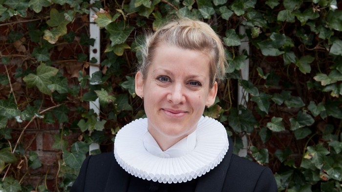 Kvinde med hvid krage står foran grønne planter