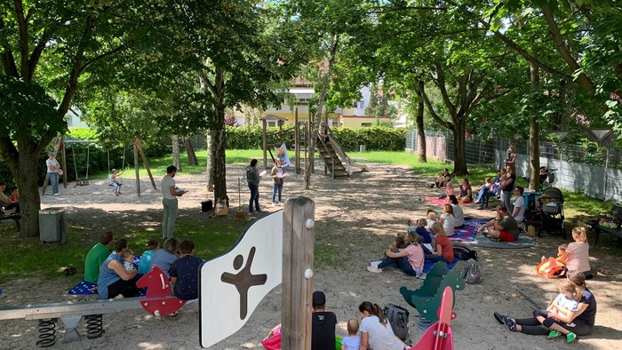 Im Park sitzen und spielen viele Kinder auf dem Boden und an Spielgeräten.