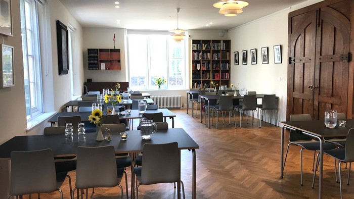 Stor, lys og moderne spiseområde med lange bord og stoler.