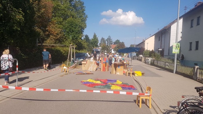 Straße abgesperrt, Kinder spielen mit bunten Hüten, Menschen schauen zu