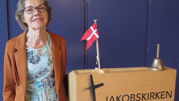 Kvinde ved podium med Jakobskirken og dansk flag