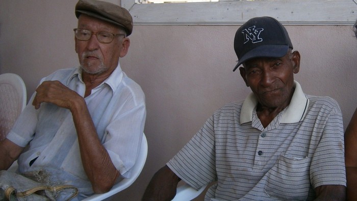 Zwei ältere Männer sitzen nebeneinander und schauen in die Kamera.