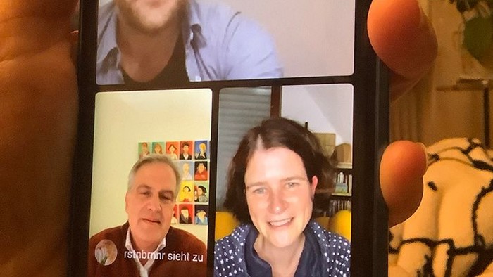 Hand hält Smartphone mit vier Personen in Videoanruf