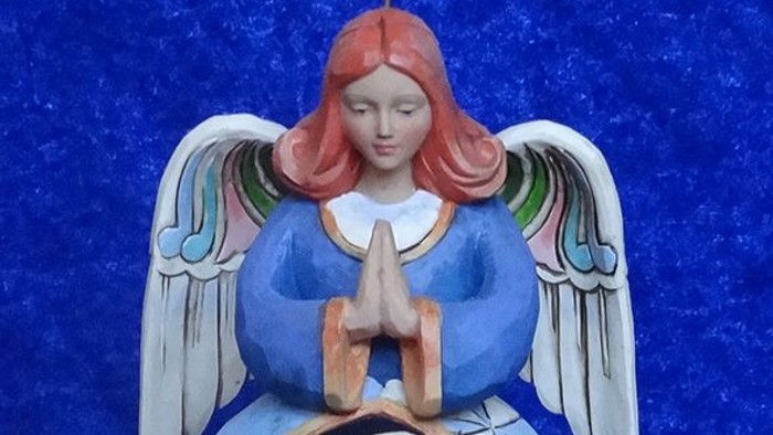 Engelsfigur mit roten Haaren und blauen Flügeln betet vor blauem Hintergrund