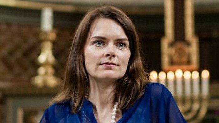 Kvinde i blå bluse sidder i kirke.