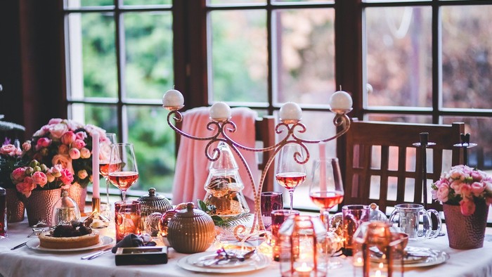Ein festlich gedeckter Tisch mit Kerzen, Blumen und Gläsern vor einem Fenster