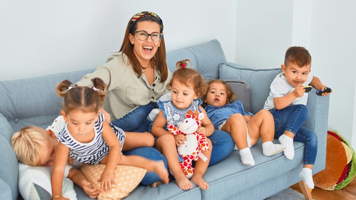 Eine Mutter sitzt mit ihren vier Kindern auf einem blauen Sofa in einem hellen Raum.