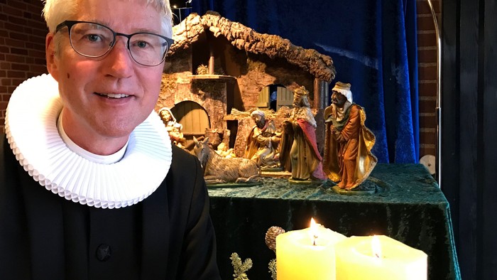 En person med hvid halsbånd står ved en julekreds med en opstilling af Jesus' fødsel