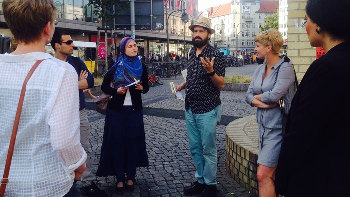 Eine Gruppe von Menschen steht auf einem Kopfsteinpflasterplatz und unterhält sich.