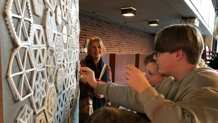 En gruppe af mennesker ser på en udstilling med geometriske mønstre på en væg.