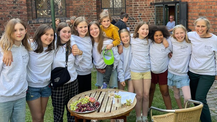 En gruppe unge piger poser sammen udenfor et murstensbygning med gotiske vinduer.