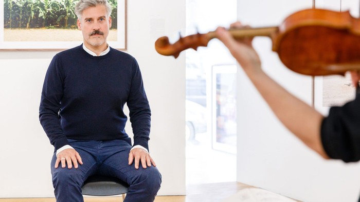 Mann sitzt und hört jemandem beim Geigen spielen