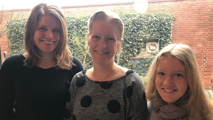Tre kvinder står sammen udenfor et murværk med klokke.