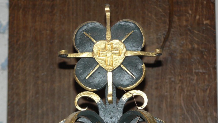 Ein goldener und schwarzer Kreuzanhänger an einer Holzwand