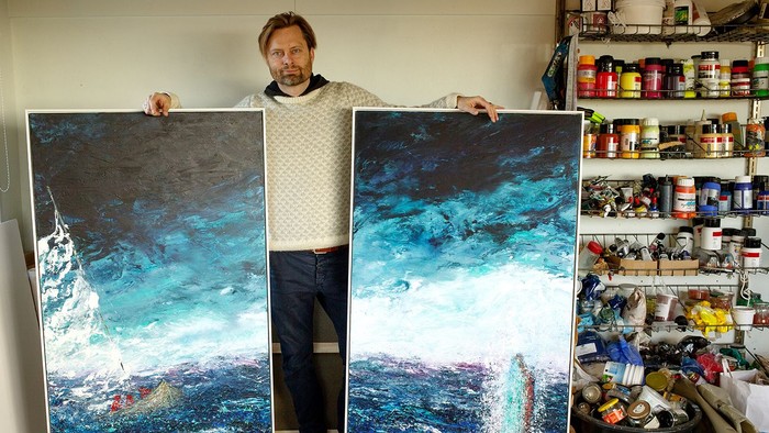Man holding two large paintings in an art studio.