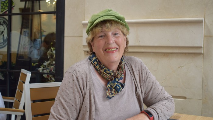 En kvinde med grøn hat og bænder om halsen sidder ved en bord udendørs