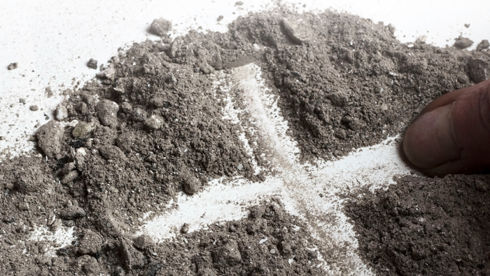 Hand drawing a cross in dirt.