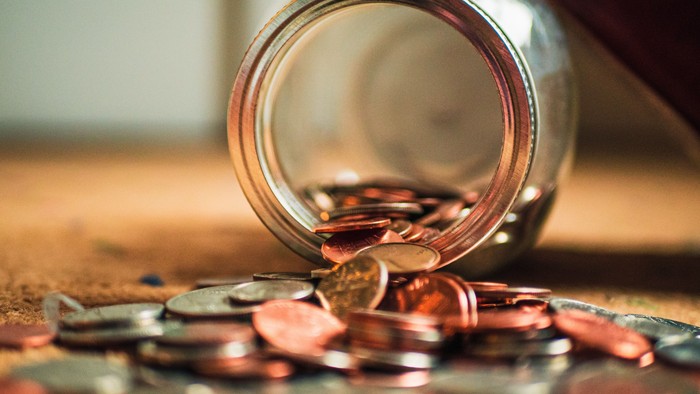 Ein Glas mit herausfallenden Münzen auf einem Holztisch