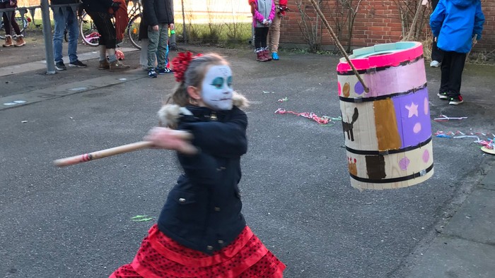 En lille pige i rødt tøj slår på en pap-pinata med en stok