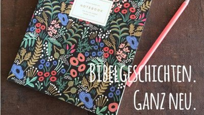 Ein buntes Notizbuch mit Blumenmuster liegt auf einem Holzboden, daneben ein roter Stift.