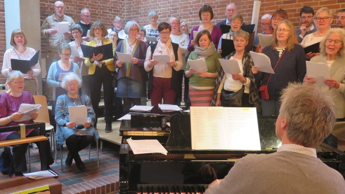 En gruppe af mennesker synger sammen med noter og en pianist spiller piano